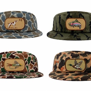 May include: Four five-panel caps featuring camouflage patterns in various colorways. Each hat has a rectangular leather-like patch on the front panel displaying embroidered illustrations of a hunting dog, a rainbow trout, a fishing fly, and a mallard duck.