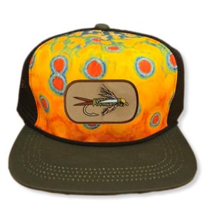 May include: A yellow, orange, and blue trucker hat with a black mesh back. The hat has a brown patch with a colorful fly fishing lure on it.