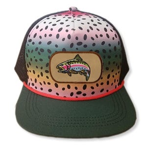 May include: A green and black mesh trucker hat with a rainbow trout patch. The hat has a pink and white spotted pattern.