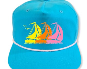 May include: A turquoise blue baseball cap with a white rope trim and a graphic of three sailboats in yellow, orange, and pink.