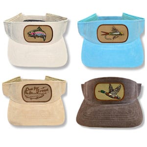 May include: Four different visor hats with embroidered patches. The first hat is beige with a rainbow trout patch. The second hat is light blue with a fly fishing lure patch. The third hat is beige with a brown patch that says "Out for Trout". The fourth hat is brown with a duck patch.