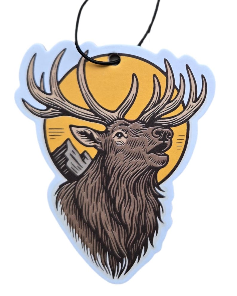 May include: An air freshener with a brown elk design. The elk has large antlers and is set against a yellow sun and mountain scene. The air freshener has a light blue border and a black string for hanging.