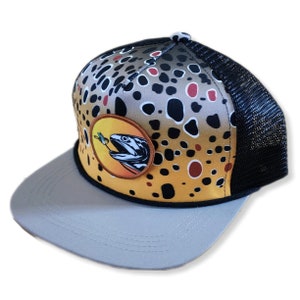 May include: A brown and black trucker hat with a brown trout fish graphic on the front. The hat has a black mesh back and a gray bill.