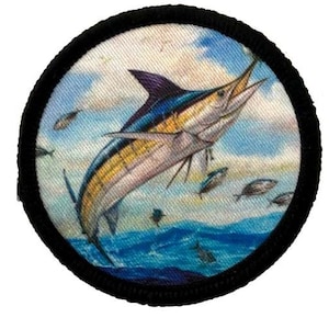 May include: A round patch with a black border and a colorful image of a marlin jumping out of the water. The marlin is blue, yellow, and white with a black dorsal fin. The background is a blue and white sky with a few small fish swimming around the marlin.