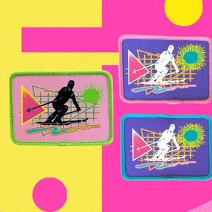 Könnte beinhalten: Zwei rosa und violette Bügelbilder mit einem Retro-Design aus den 80er Jahren, das einen Skifahrer in einem geometrischen Muster mit einem rosa Dreieck, einem grünen Kreis und einem blauen Gitter zeigt.
