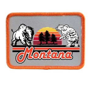 May include: A gray and orange embroidered patch with a white silhouette of a buffalo and a bear on either side of a sunset with three pine trees. The text "Montana" is written in a red retro font.