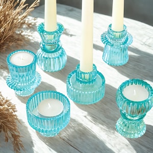 May include: A collection of teal glass candle holders and votives. The holders have ribbed detailing and hold white candles. The arrangement includes various shapes and sizes, creating a decorative display for home decor.