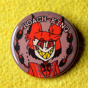 May include: A red and black button with a cartoon image of a red-haired character with a devilish grin. The character is wearing a red suit and a black bow tie. The text "ROACH KING" is written in a white circle around the character.