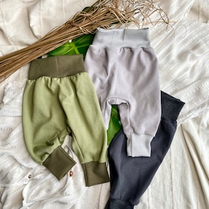 Könnte beinhalten: Drei Paar Baby- oder Kleinkind-Jogginghosen in Grün, Grau und Schwarz. Die Jogginghosen sind aus einem weichen, bequemen Stoff gefertigt und haben eine lockere Passform.