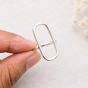 May include: A silver ring featuring a vertical, elongated rectangular frame design. The metal band is thin and smooth, forming a continuous open shape that extends upwards from the finger. The surface of the silver is polished and reflective.