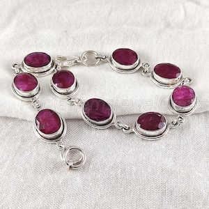 Puede incluir: Un brazalete de plata con piedras preciosas de rubí de forma ovalada. El brazalete tiene un cierre de langosta.