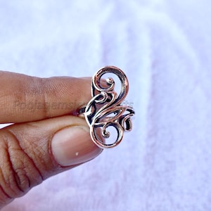 Puede incluir: Un anillo de plata con un diseño delicado e intrincado que presenta patrones en espiral que se asemejan a flores. El anillo está hecho de plata de ley y tiene un acabado pulido.