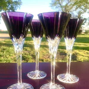 May include: Set of four purple stemmed martini glasses with a clear crystal base. The glasses have a wide, shallow bowl and a long, slender stem.