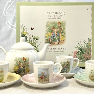 May include: A Peter Rabbit porcelain tea set, including a teapot, cups, and saucers. The set features illustrations of Peter Rabbit and other characters. The box reads "Peter Rabbit Designed Exclusively by pottery barn kids".