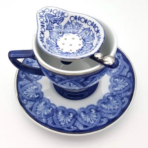 May include: A blue and white porcelain teacup and saucer set with a matching tea infuser. The set features a delicate floral design with a silver trim.
