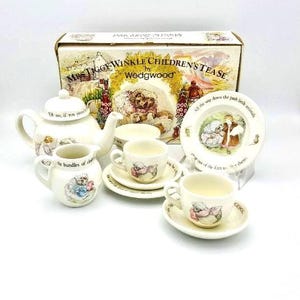 May include: A white porcelain children's tea set with a floral design featuring the characters from the book "Mrs. Tiggy-Winkle" by Beatrix Potter. The set includes a teapot, creamer, sugar bowl, two teacups, and two saucers. The box is labeled "Mrs. Tiggy-Winkle Children's Tease by Wedgwood".