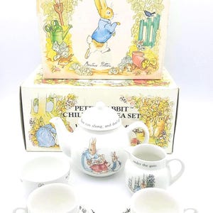 May include: A Peter Rabbit Children's Tea Set by Wedgwood. The set includes a teapot, creamer, sugar bowl, two cups, and saucers. The box and tea set feature illustrations of Peter Rabbit and other characters.