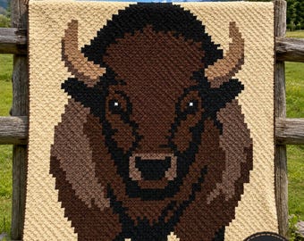 May include: A crochet blanket featuring a pixelated buffalo design in shades of brown, black, and tan. The text at the top reads Buffalo CROCHET BLANKET PATTERN, and a circular badge in the bottom right corner reads Instant PDF Download.