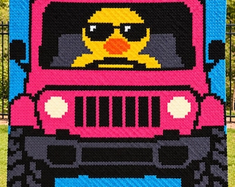 May include: A crochet blanket featuring a pixelated design of a bright pink off-road vehicle against a blue background. A yellow duck wearing black sunglasses is visible in the driver's seat. The vehicle has black tires, a black grille, and white headlights.