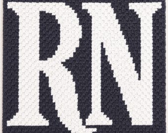 May include: A dark gray crocheted blanket featuring the large white letters RN in a blocky, pixelated style. The textile has a consistent square-stitch pattern throughout, creating a textured surface with high contrast between the letters and background.