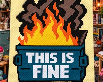May include: A rectangular crochet blanket with a light yellow background featuring a pixelated blue dumpster on fire. Bright orange and yellow flames rise from the dumpster with dark gray smoke above. The text THIS IS FINE is in white.