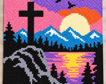 May include: A rectangular crochet blanket featuring a pixelated landscape design. The scene depicts a black cross on a hill, blue mountains with white peaks, a yellow sun, and a purple sky with black birds. A lake reflects the sunset colors.