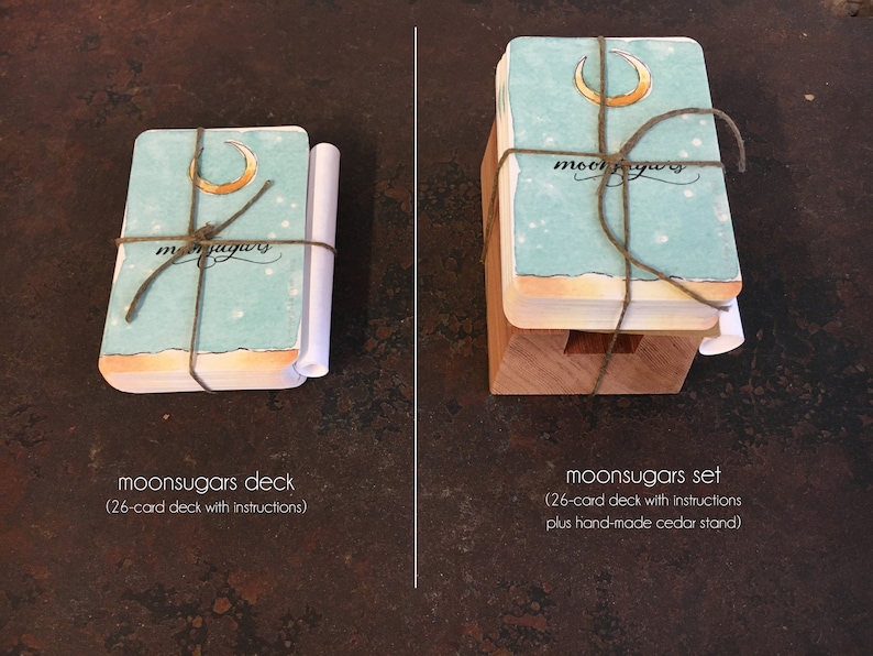 May include: Two versions of a moonsugars deck of cards. The deck on the left is wrapped in twine and includes instructions. The deck on the right is on a wooden stand and includes instructions. Both decks feature a crescent moon and the word "moonsugars" on the front.