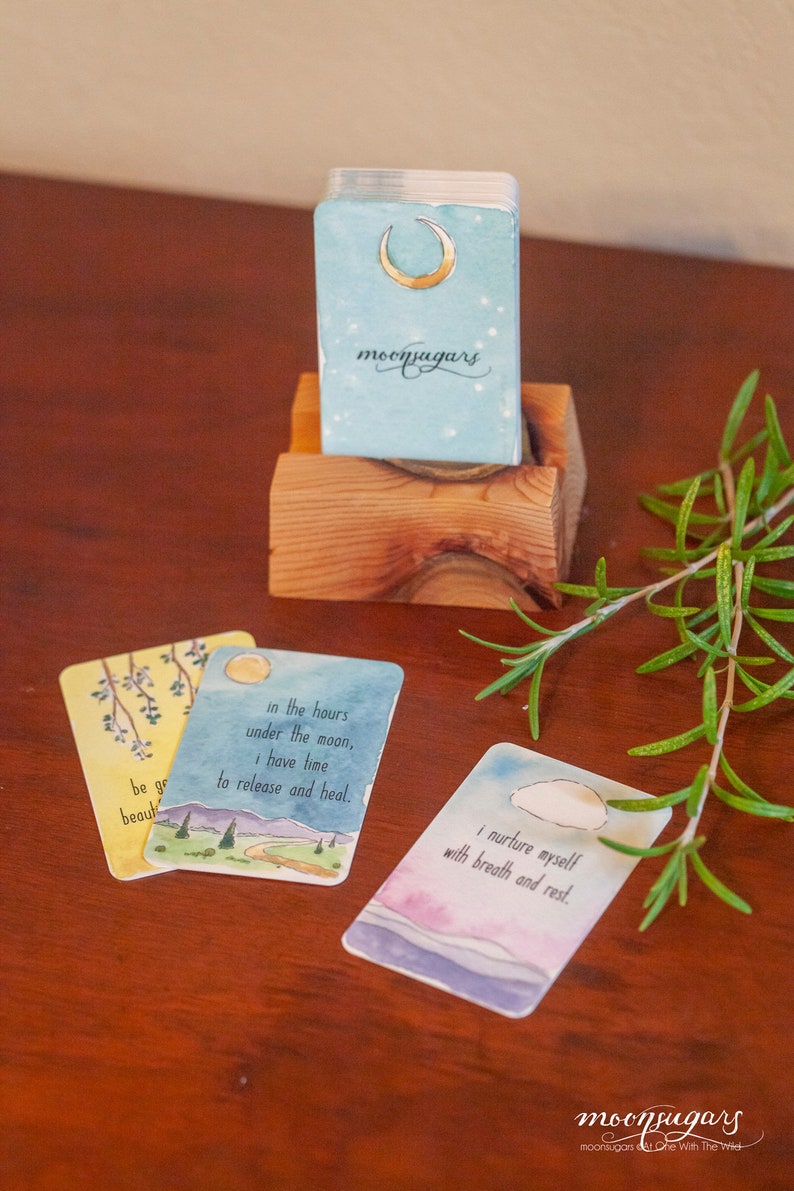 May include: Three watercolor cards with inspirational quotes about self-care and healing. The cards feature a crescent moon, a mountain range with a winding path, and a cloud in a blue sky. The cards are part of a deck called "moonsugars".