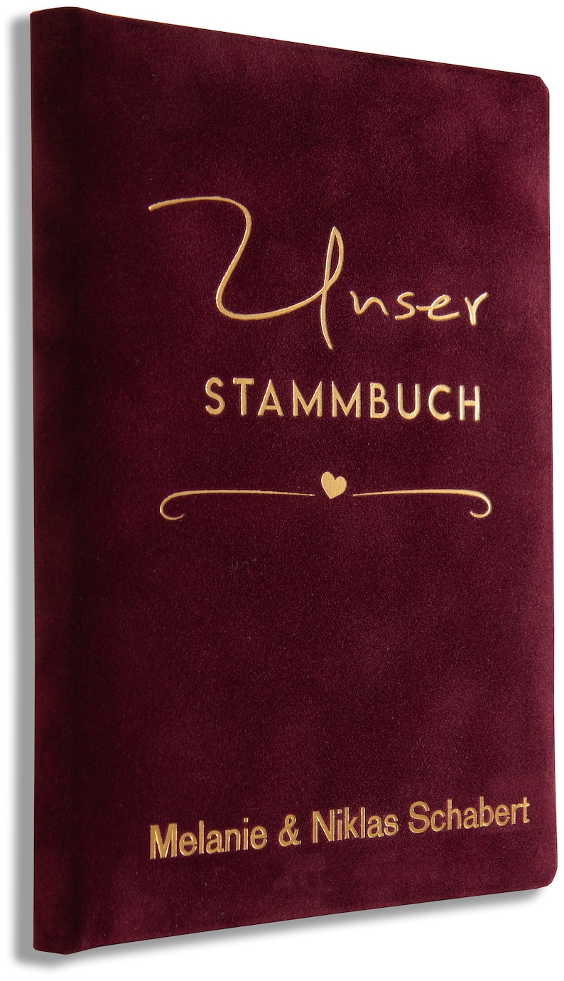 May include: Burgundy velvet book with gold lettering that reads "Unser Stammbuch" with a small heart and the names "Melanie & Niklas Schabert".