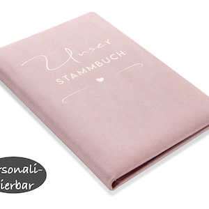 Könnte beinhalten: Ein pinkfarbenes Buch mit einem Bezug aus Wildleder, auf dem in weißer Schrift "Unser Stammbuch" steht. Das Buch ist mit einem kleinen weißen Herz personalisiert.