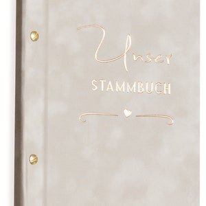 May include: A beige fabric-covered album with gold accents. The front cover features the text "Unser Stammbuch" with a small heart symbol.