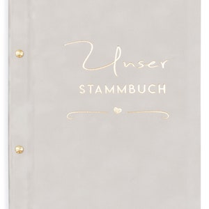 May include: A gray, soft-cover book with the text "Unser Stammbuch" in gold lettering. A small gold heart is above a decorative gold swirl.