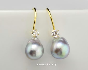May include: A pair of gold drop earrings featuring iridescent, teardrop-shaped gray pearls suspended from small, clear, round-cut stones. The earrings are displayed against a white surface with the text Jennita Luxury printed below.