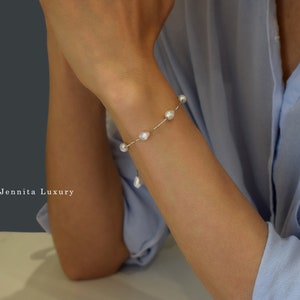 Op de afbeelding: Een delicate armband met een zilveren ketting en witte parel accenten. De armband wordt getoond op de pols van een persoon.