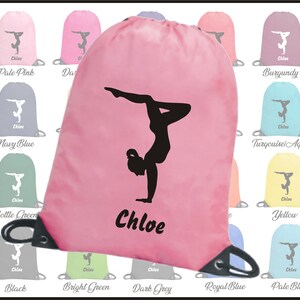 Peut inclure: Un sac &agrave; cordon rose avec une silhouette noire d'une gymnaste faisant un poirier. Le sac a un cordon noir et le nom "Chloe" est imprim&eacute; en noir sur le devant.