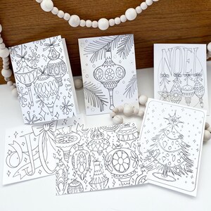 May include: Five black and white printable Christmas cards featuring various holiday designs. The cards include ornaments, a Christmas tree, and the word "NOEL".