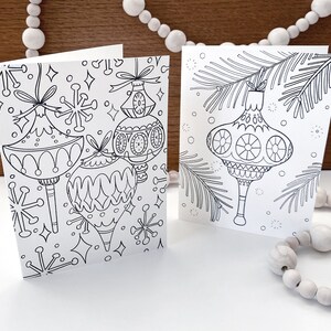 May include: Two blank coloring cards featuring Christmas ornaments. The first card has three ornaments with snowflake and star designs. The second card has one ornament with a pine branch design.