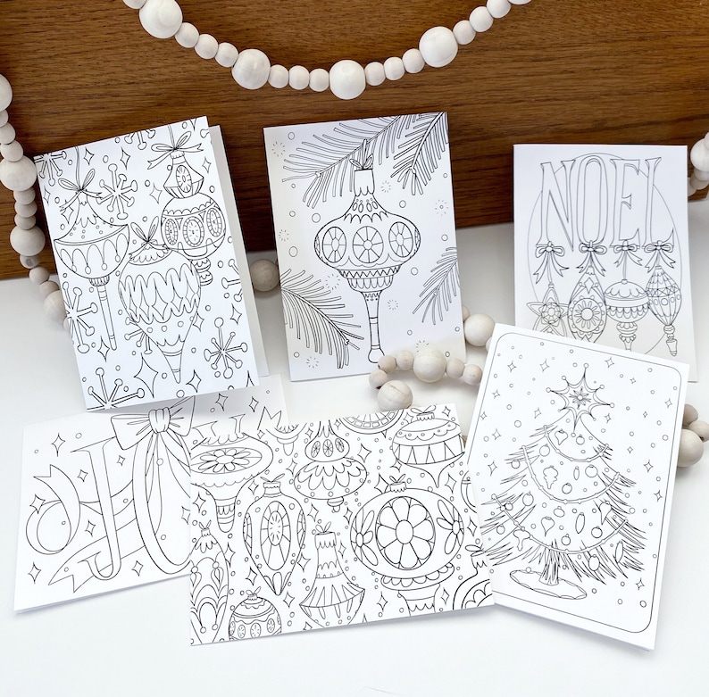 May include: Five black and white printable Christmas cards featuring various holiday designs. The cards include ornaments, a Christmas tree, and the word "NOEL".