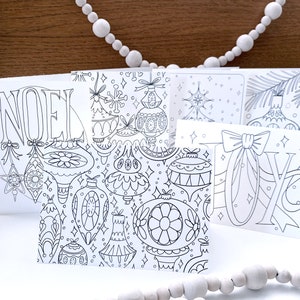 May include: A set of five printable Christmas cards featuring black and white illustrations of ornaments, stars, and the words "Noel" and "Joy".