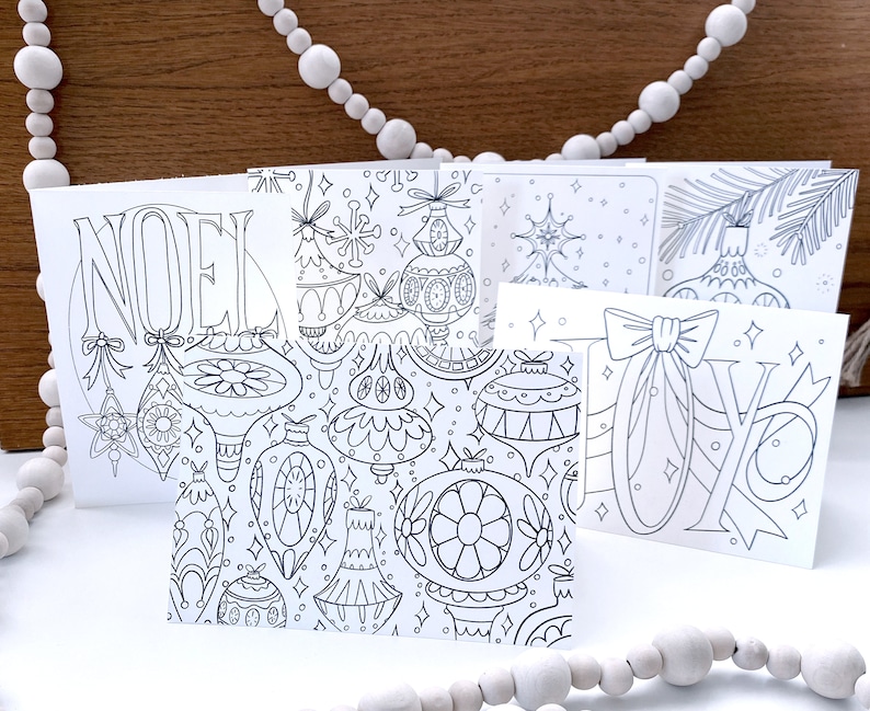 May include: A set of five printable Christmas cards featuring black and white illustrations of ornaments, stars, and the words "Noel" and "Joy".