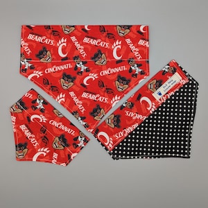 May include: A set of three pet bandanas. Two bandanas are red with a repeating pattern of the word "Bearcats", the letter "C", and a cartoon bear. The third bandana is black with white polka dots and a red border.