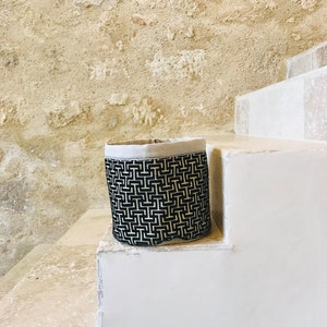 Può includere: Un cesto di stoffa per la conservazione con motivo geometrico bianco e nero con un bordo superiore bianco. Il cesto è seduto su un set di scale bianche.