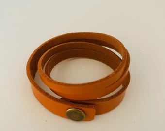 May include: A tan leather wrap bracelet featuring a smooth exterior and a textured interior. The bracelet is designed to wrap around the wrist multiple times and is secured with a single, circular, antique-style brass metal snap button fastener.