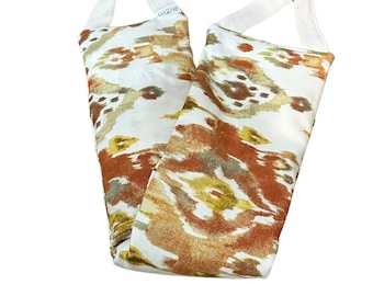 May include: Two white fabric bags with orange, brown, and green ikat pattern. The bags have white straps and are made for heating.