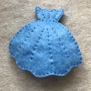 May include: A blue felt dress with a scalloped edge and stitched details. The dress is a simple design with a rounded shape.