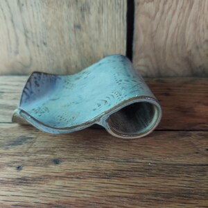 Könnte beinhalten: Eine handgefertigte Seifenschale aus Keramik mit einem einzigartigen, geschwungenen Design. Die Schale hat eine hellblaue Glasur mit braunen Rändern und eine strukturierte Oberfläche. Die Seifenschale ist ca. 15 cm lang.