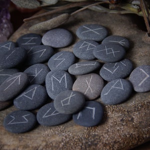 May include: A set of gray stones with white runes painted on them. The stones are arranged in a circle on a wooden surface.
