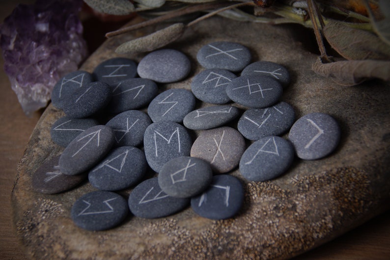 May include: A set of gray stones with white runes painted on them. The stones are arranged in a circle on a wooden surface.