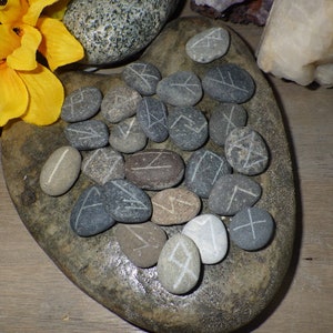 May include: A heart-shaped stone with 25 gray and brown stones with white runes carved on them.