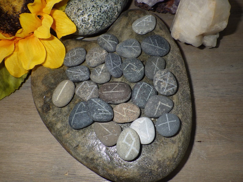 May include: A heart-shaped stone with 25 gray and brown stones with white runes carved on them.